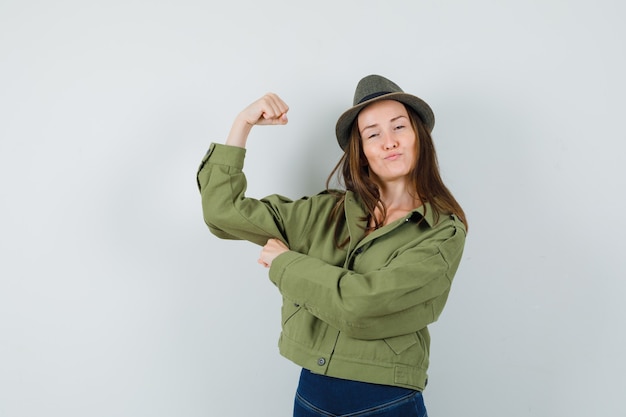 Jeune femme montrant les muscles du bras en chapeau de pantalon veste et à la confiance