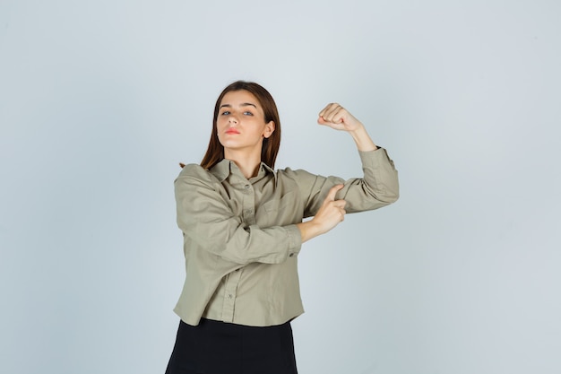 Jeune femme montrant les muscles du bras en chemise, jupe et à la confiance