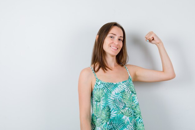 Jeune femme montrant les muscles du bras et semblant joyeuse. vue de face.