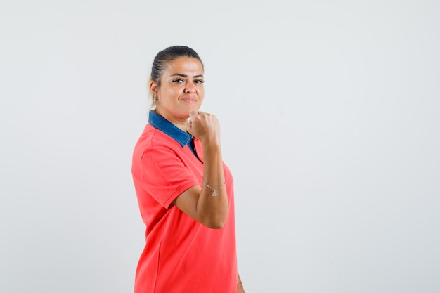 Jeune femme montrant les muscles en t-shirt rouge et à la puissante, vue de face.