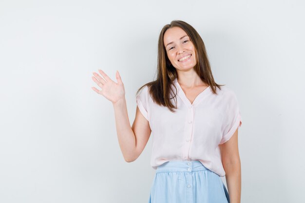 Jeune femme montrant la paume en t-shirt, jupe et à la joie. vue de face.