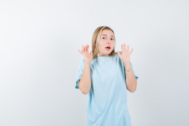 Jeune femme montrant des paumes dans un geste d'abandon en t-shirt et à la perplexité. vue de face.