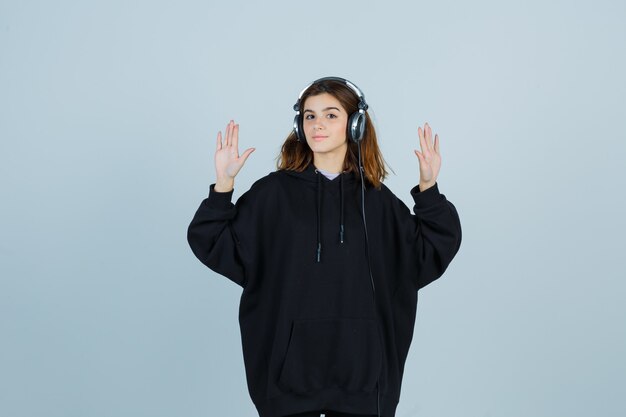 Jeune femme montrant des paumes dans un sweat à capuche surdimensionné, un pantalon et une charmante vue de face.