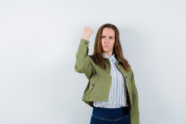 Jeune femme montrant le poing fermé en chemise, veste et à la rancune. vue de face.