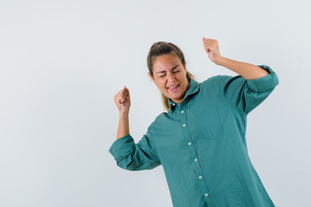 Jeune femme montrant la pose du gagnant en chemisier vert et à la jolie