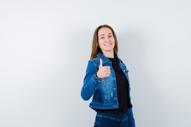 Jeune femme montrant le pouce en chemise, veste et l'air confiant. vue de face.