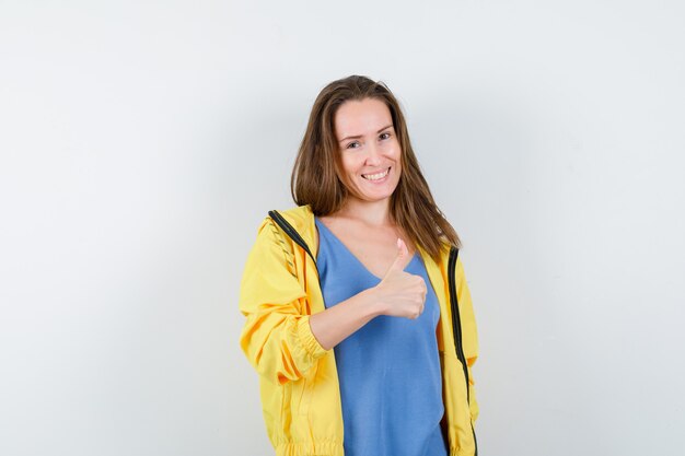 Jeune femme montrant le pouce en t-shirt, veste et l'air confiant. vue de face.