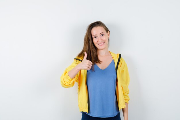 Jeune femme montrant le pouce en t-shirt, veste et à la recherche de joyeux. vue de face.