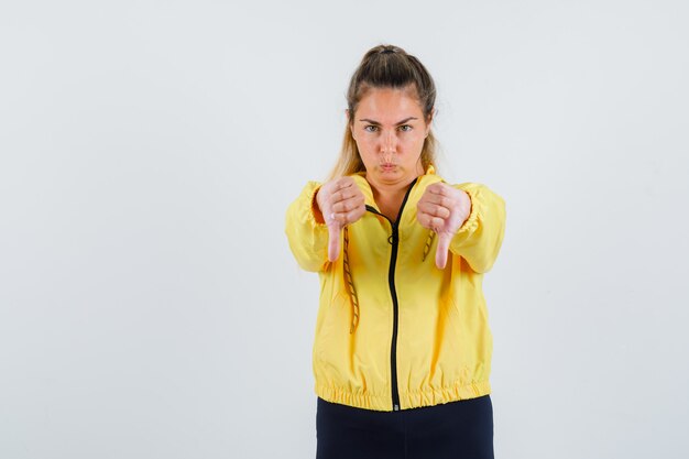 Jeune femme montrant le pouce vers le bas en imperméable jaune et à la mécontentement