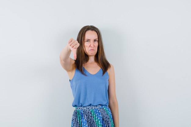 Jeune femme montrant le pouce vers le bas en maillot, jupe et à l'insatisfaction, vue de face.