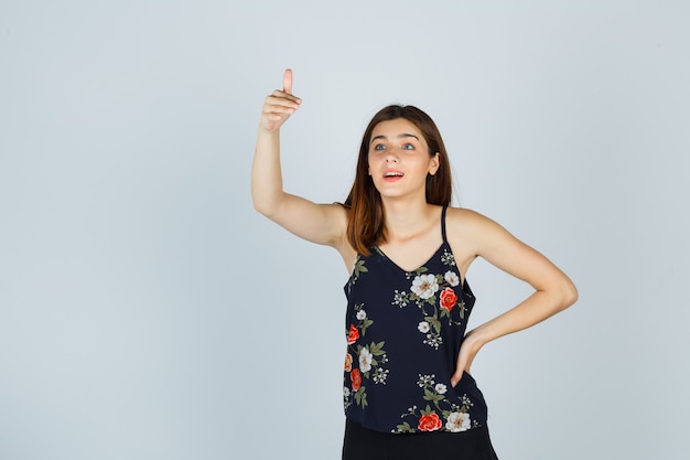 Jeune femme montrant le pouce vers le haut en chemisier et à la demande, vue de face.