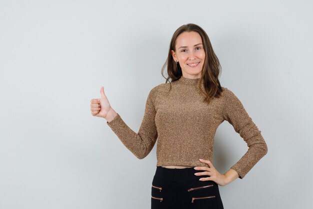 Jeune femme montrant le pouce vers le haut en chemisier doré et à la confiance en soi. vue de face.