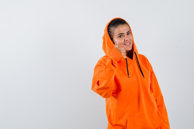 Photo gratuite jeune femme montrant le pouce vers le haut dans un sweat à capuche orange et à la belle