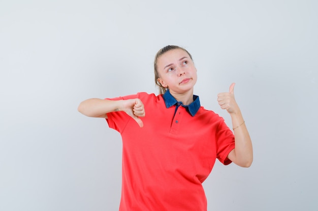 Jeune femme montrant les pouces de haut en bas en t-shirt et à l'hésitation