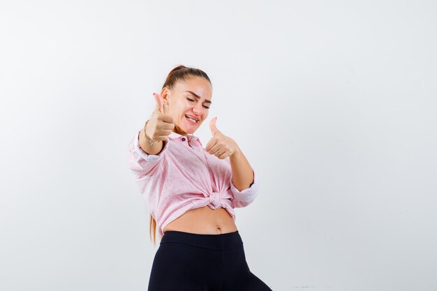 Jeune femme montrant les pouces vers le haut en chemise, pantalon et air heureux