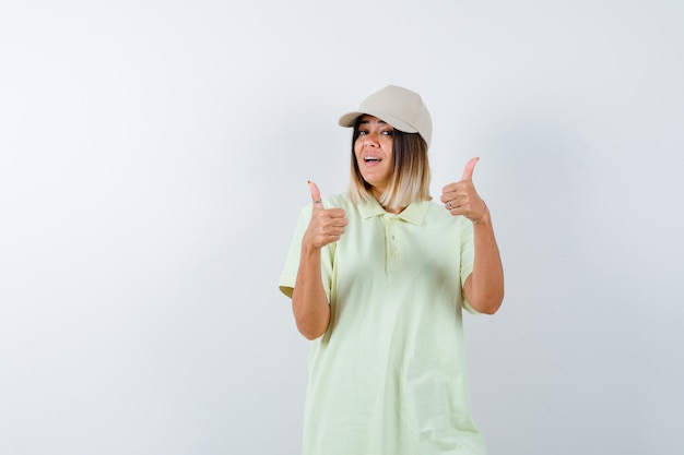 Jeune femme montrant les pouces vers le haut en t-shirt, casquette et à la recherche positive. vue de face.