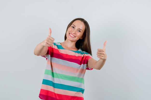 Jeune femme montrant les pouces vers le haut en t-shirt et à la joyeuse vue de face.