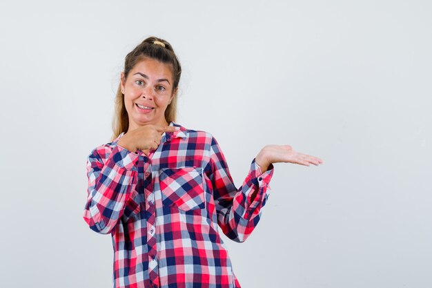 Jeune femme montrant quelque chose qui faisait semblant d'être tenu en chemise à carreaux et avait l'air joyeux. vue de face.