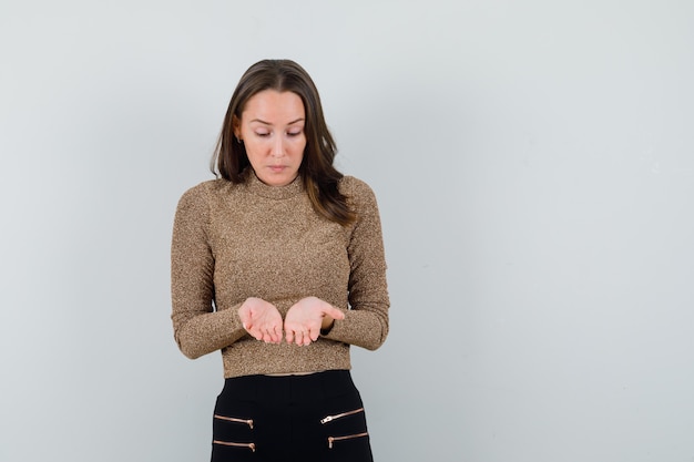 Jeune femme montrant quelque chose à sa main en chemisier doré et à la vue de face, focalisée. espace pour le texte