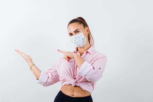 Jeune femme montrant sa paume de côté en chemise, masque et à la vue de face confiante.