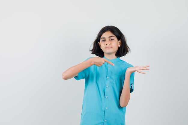 Jeune femme montrant sa paume ouverte en chemise bleue et à l'air ravie.