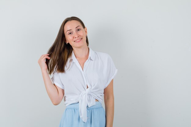 Jeune femme montrant ses cheveux tout en souriant en chemisier et jupe et à la mignonne