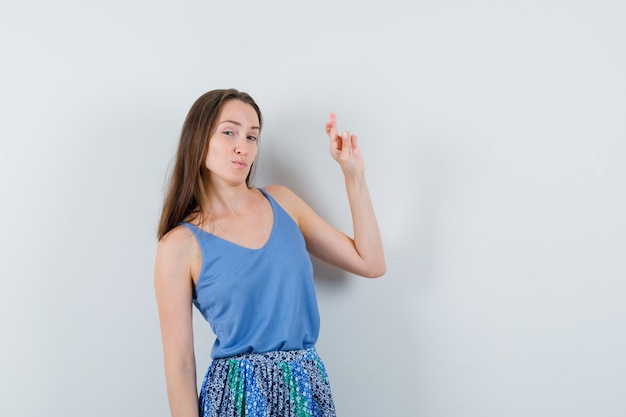 Jeune femme montrant ses doigts croisés en chemisier bleu, jupe et à la vue de face confiante