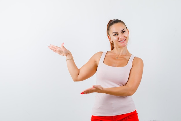 Jeune femme montrant un signe de grande taille en débardeur beige et à la joyeuse vue de face.