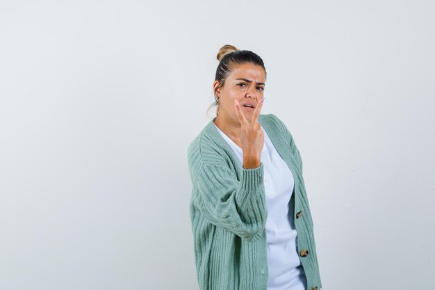 Jeune femme montrant le signe de la paix en chemise blanche et cardigan vert menthe et à la grave