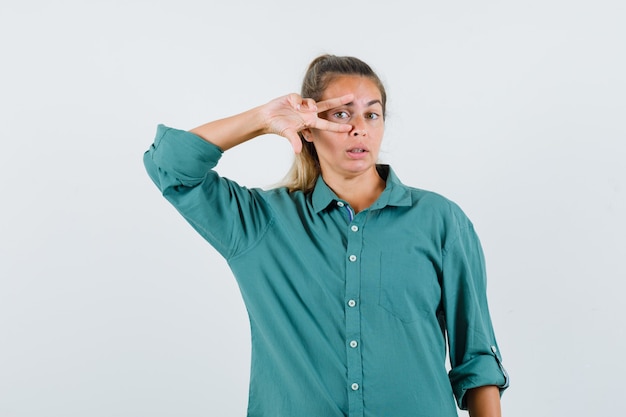 Jeune femme montrant le signe v sur l'oeil en chemisier vert et à la grave