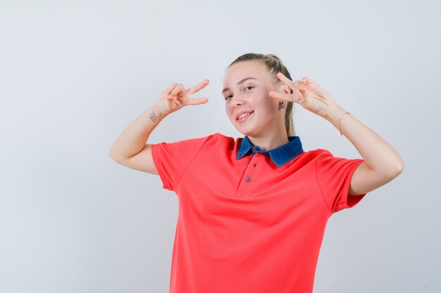 Jeune femme montrant v-sign en t-shirt et à la joyeuse