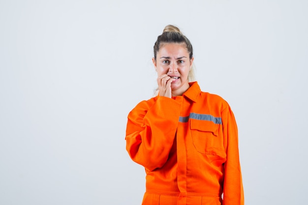 Jeune femme mordant ses doigts en uniforme de travailleur et à la vue de face, nerveuse.