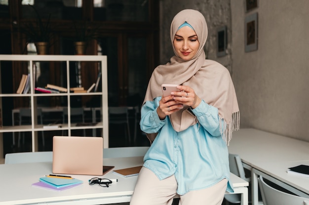 Jeune femme musulmane assez moderne en hijab travaillant dans un bureau, éducation en ligne