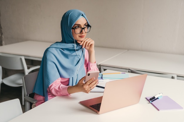 Jeune femme musulmane assez moderne en hijab travaillant sur ordinateur portable dans la salle de bureau, éducation en ligne