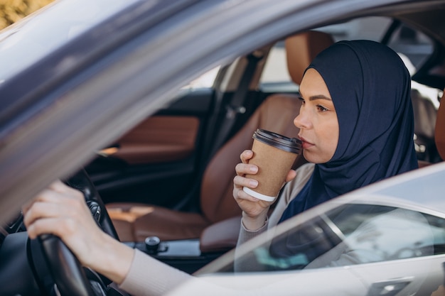 Jeune femme musulmane moderne buvant du café en voiture