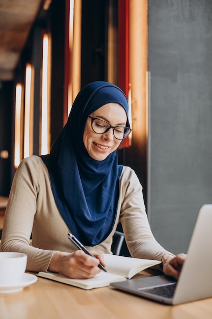 Jeune femme musulmane travaillant en ligne sur ordinateur dans un café