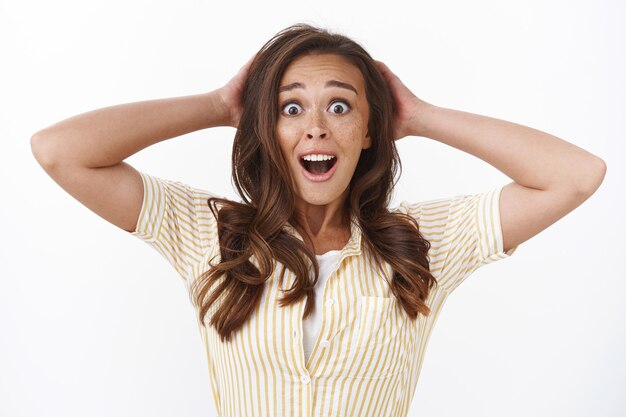 Jeune femme nerveuse surprise en gros plan avec des taches de rousseur, recevoir des nouvelles inattendues, mâchoire tombante haletante choquée, saisir la tête étonnée, regarder la caméra avec les sourcils rasés d'étonnement