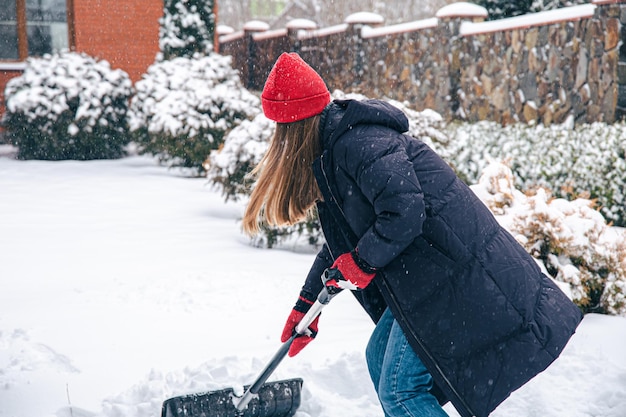 La jeune femme nettoie la neige dans la cour par temps neigeux