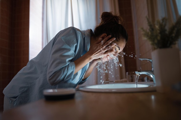 Photo gratuite jeune femme nettoyant son visage avec de l'eau dans la salle de bain