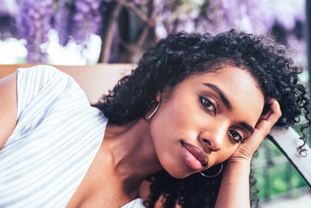 Jeune femme noire allongée sur une chaise entourée de fleurs