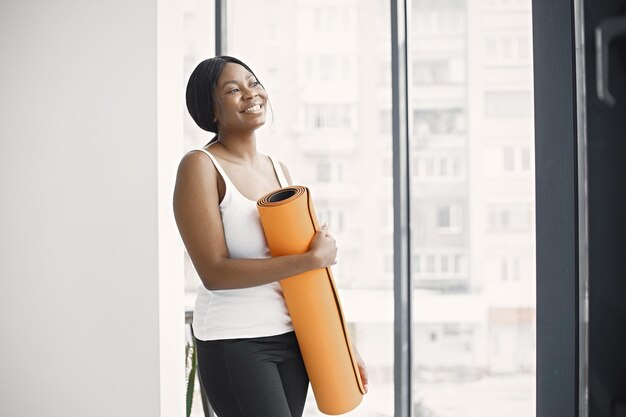 Jeune femme noire prête pour l'entraînement tenant un tapis de yoga orange