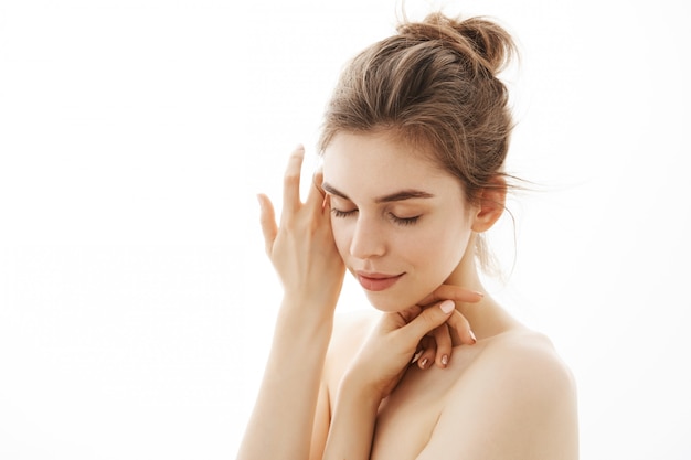 Jeune femme nue tendre avec chignon posant sur fond blanc. Yeux fermés.