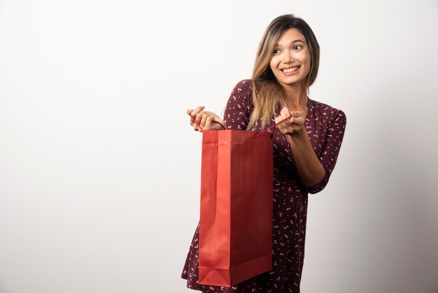 Jeune femme ouvrant un sac à provisions sur un mur blanc.