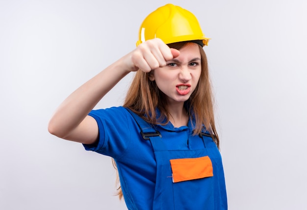 Jeune femme ouvrier constructeur en uniforme de construction et casque de sécurité serrant le poing à l'avant