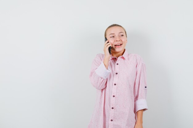 Jeune femme parlant au téléphone mobile en chemise rose et à la joyeuse