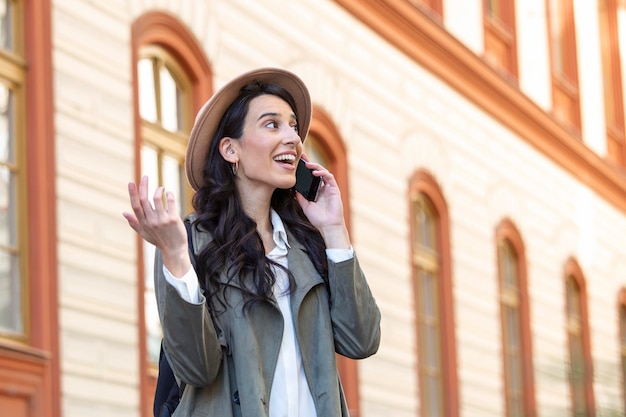 Photo gratuite jeune femme parlant au téléphone mobile et en détournant les yeux fille réussie dans les appels occasionnels sur smartphone dans la ville tout en se tenant sur le trottoir