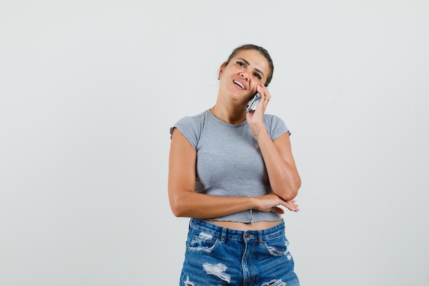 Jeune femme parlant au téléphone mobile en t-shirt, short et à la recherche d'optimiste.