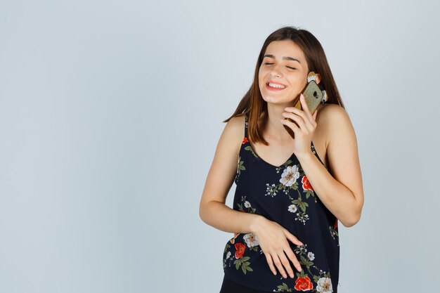 Jeune femme parlant au téléphone portable en blouse et regardant joyeuse, vue de face.
