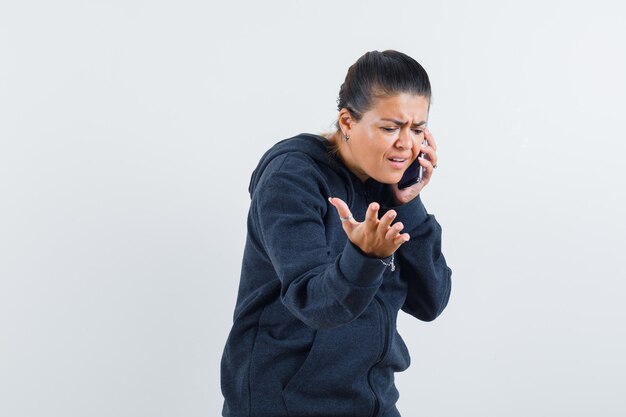 Jeune femme parlant au téléphone portable en veste et à la nervosité. vue de face.