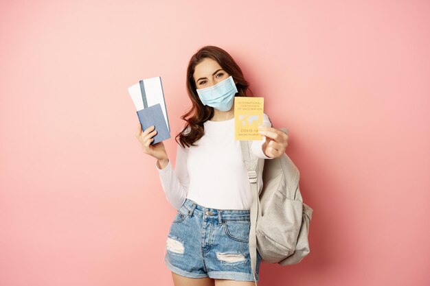Jeune femme partant en voyage portant un masque médical montrant un passeport de certificat covid et un ticket d'aiplance...